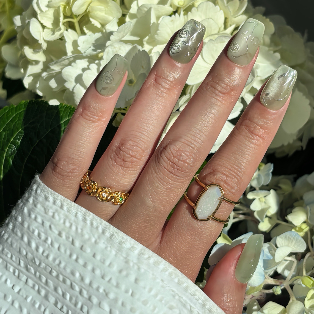 Pinkie Promise Nails Press-Ons Reusable Best Press-on Nails Salon Quality Nails at home Jade Medium Squoval Hand Image Build Your Kit Press-On Nails, Hand with green flower decorative nails and rings in front of white flowers